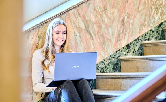 Person sitting on a staircase with a laptop on their lap.